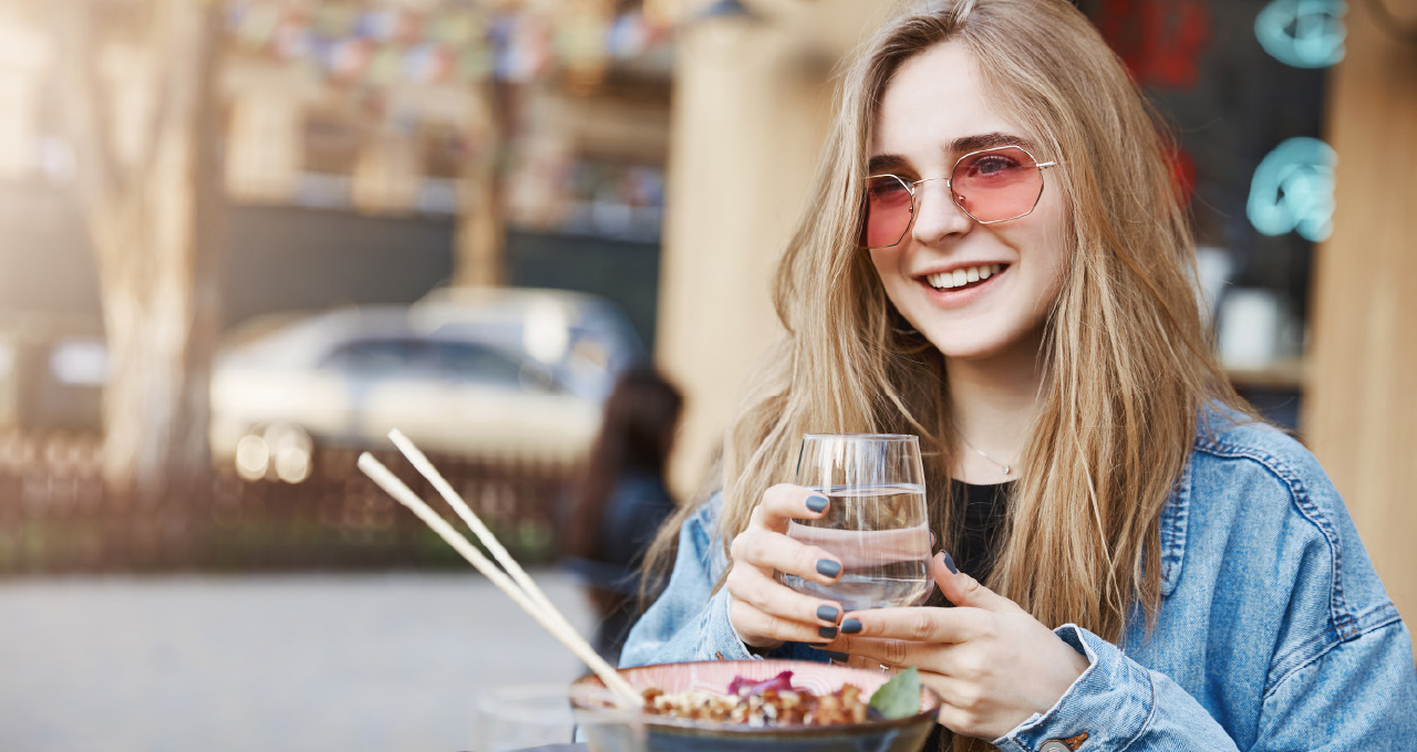 Frau mit Wasserglas in der Hand und roter Sonnenbrille