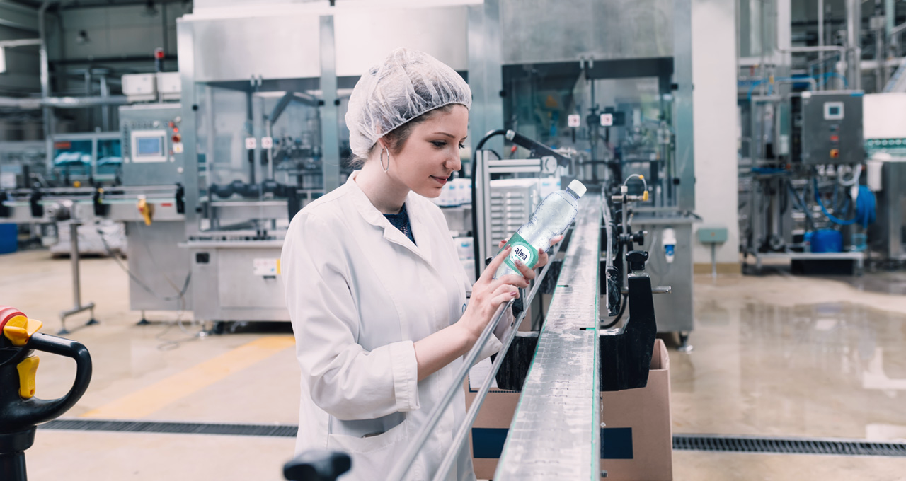 Frau prüft Flasche mit Mineralwasser medium in der Produktion