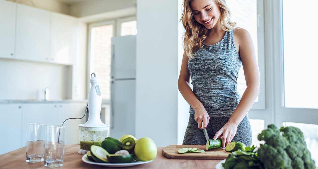 Sportliche Frau schneidet Gurken in der Küche