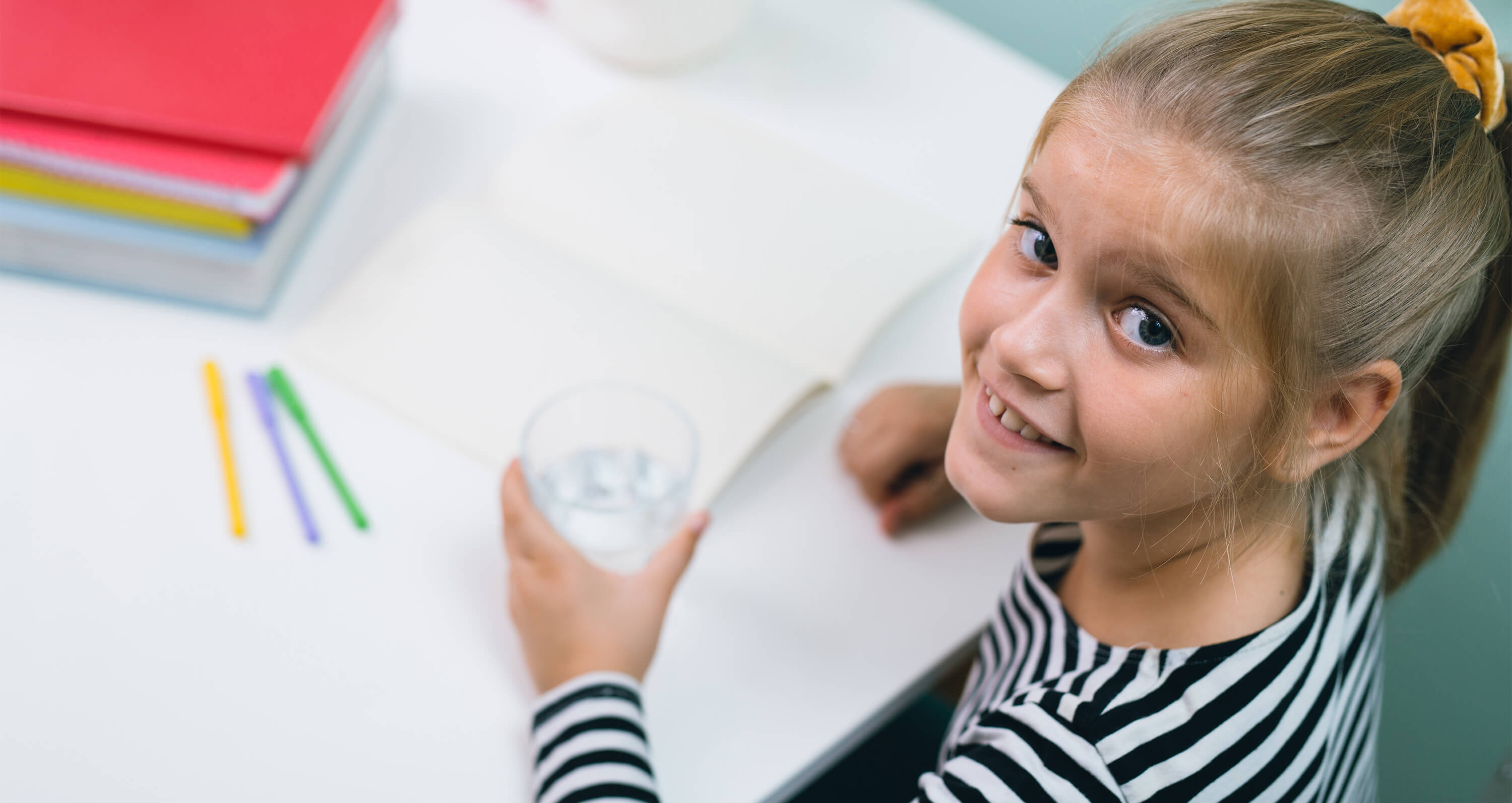 Mädchen mit Mineralwasserglas an Schreibtisch